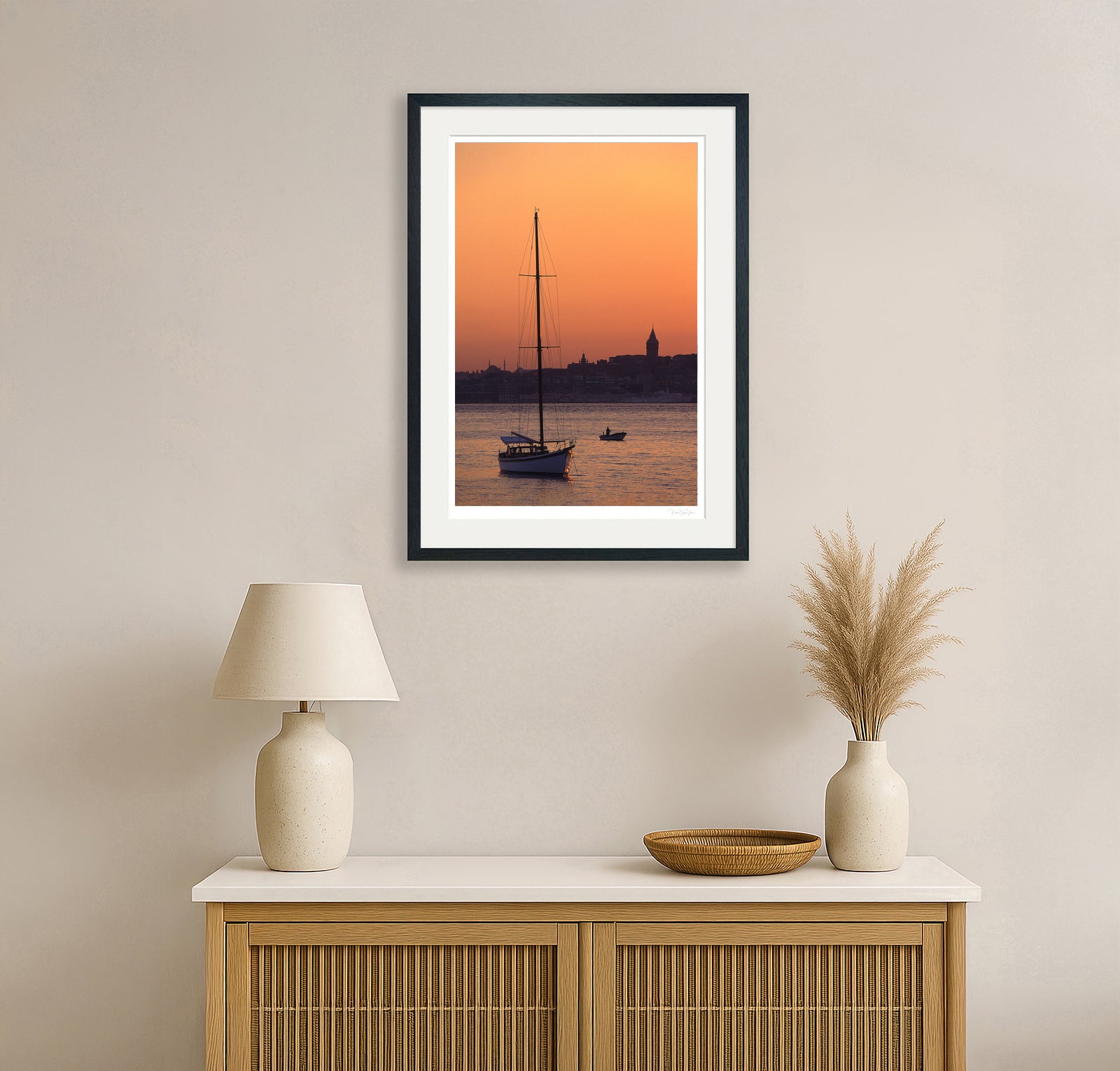 Sailboat at sunset fine art print framed and displayed above a minimalist wooden cabinet in warm-toned room