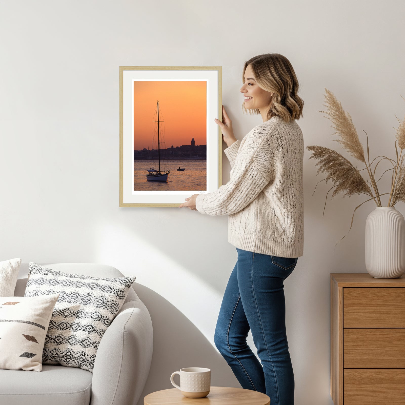 Woman displaying Istanbul sunset art print with sailboat and Galata Tower in natural wood frame