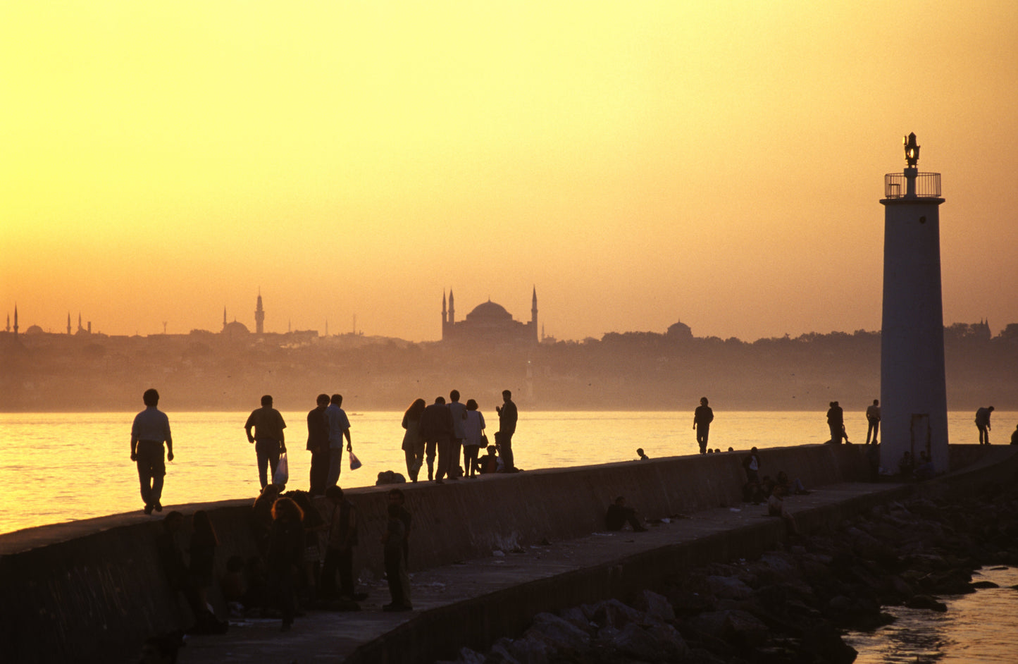 Silhouettes of people strolling along Istanbul's waterfront breakwater at golden sunset, with Hagia Sophia and the historic mosque skyline across the Bosphorus, fine art photography print
