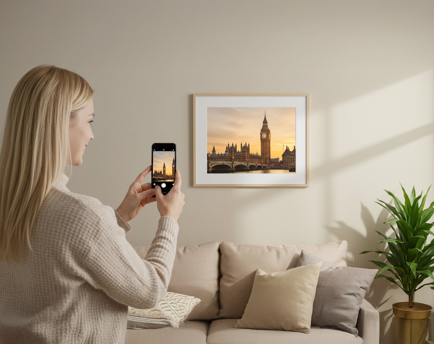 A smiling woman captures her framed Big Ben print on her phone in a cosy living room – showcasing how personal photos can be turned into elegant wall art.