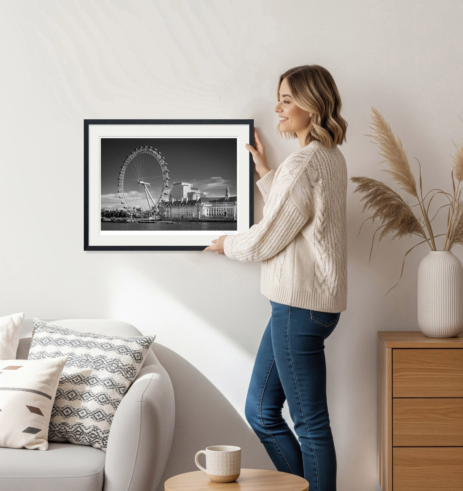 Woman hanging framed London Eye fine art print in a modern living room – black and white city wall decor