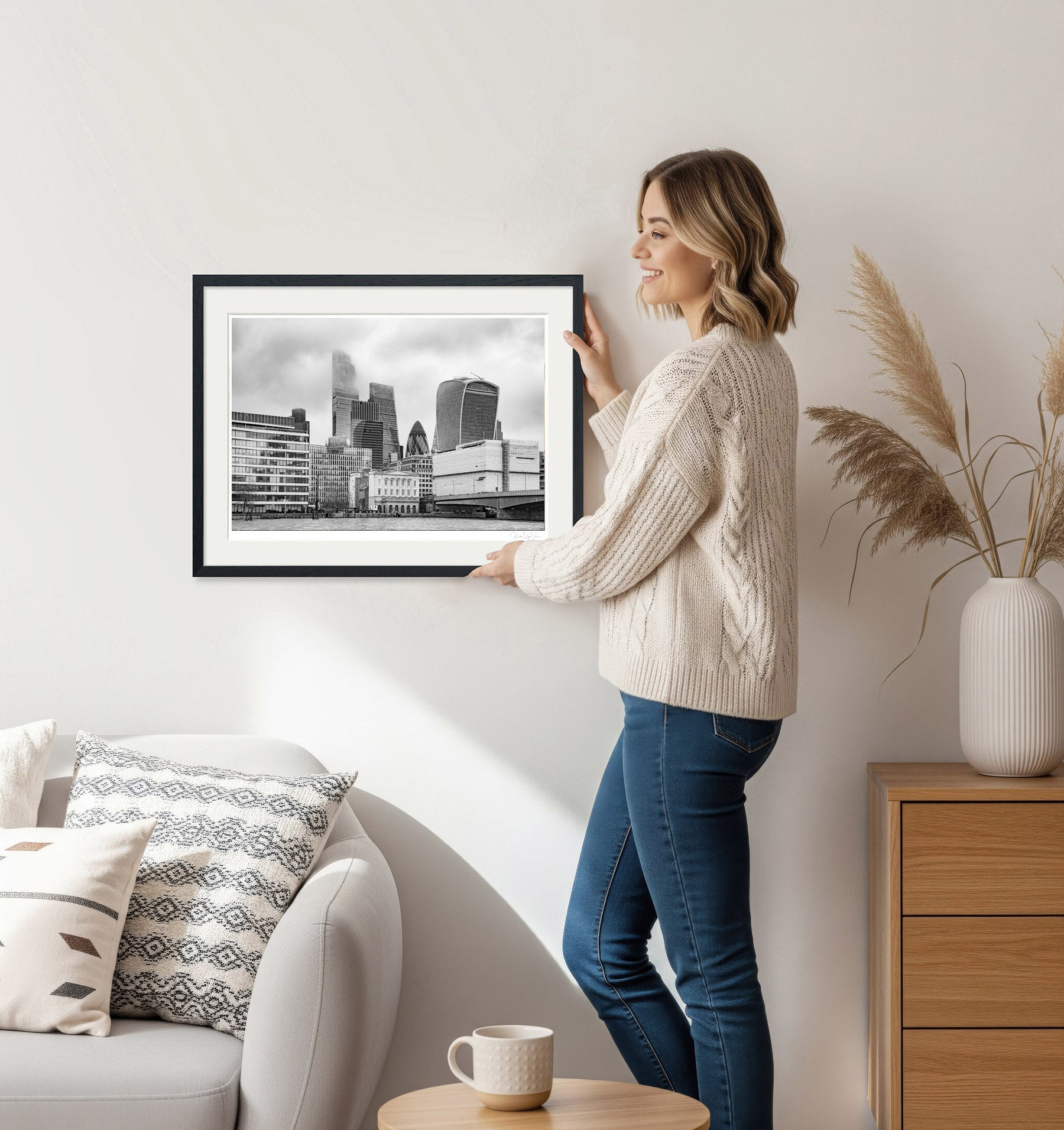 Woman decorating a room with a framed black and white London skyline wall art piece
