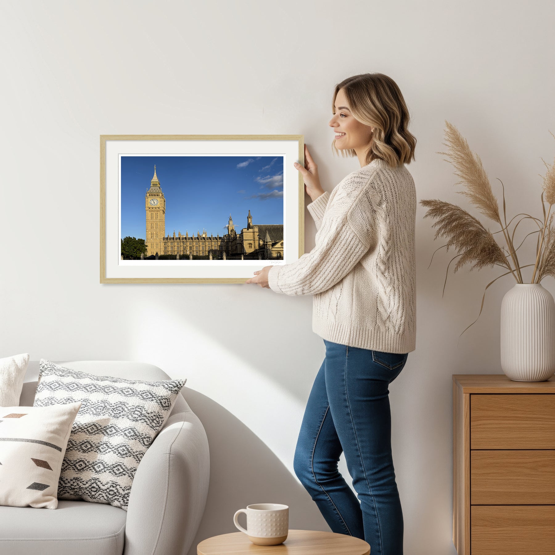 Woman holding framed Big Ben fine art print in natural wood frame, cozy interior setting