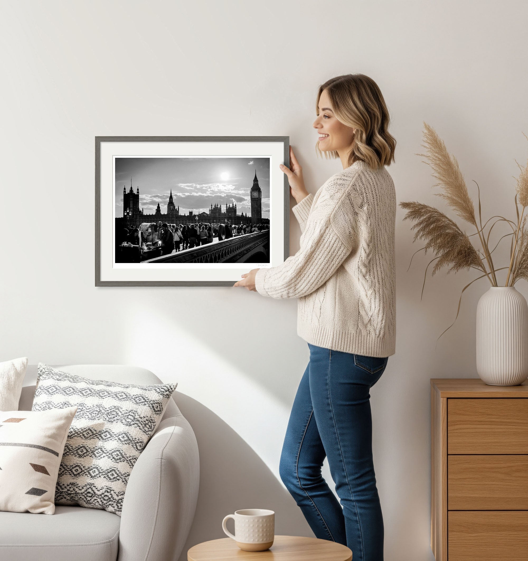 Woman holding framed black and white fine art photo of Westminster Bridge and Big Ben in a cozy home interior.