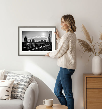 Woman holding framed black and white fine art photo of Westminster Bridge and Big Ben in a cozy home interior.