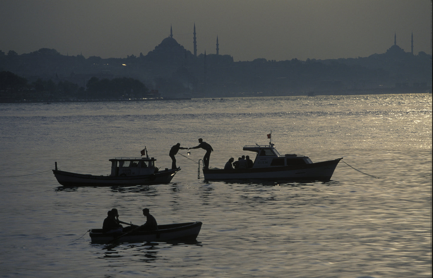 Silhouette of fishermen on three boats at dusk on the Bosphorus, with Süleymaniye Mosque and Istanbul skyline in the background, fine art photography print