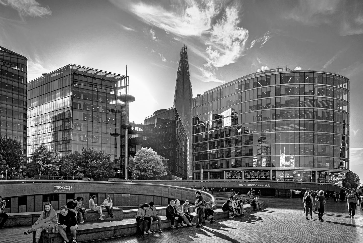 People sitting on the steps of The Scoop amphitheatre at More London Riverside with The Shard rising dramatically behind the glass office buildings, black and white fine art photography print