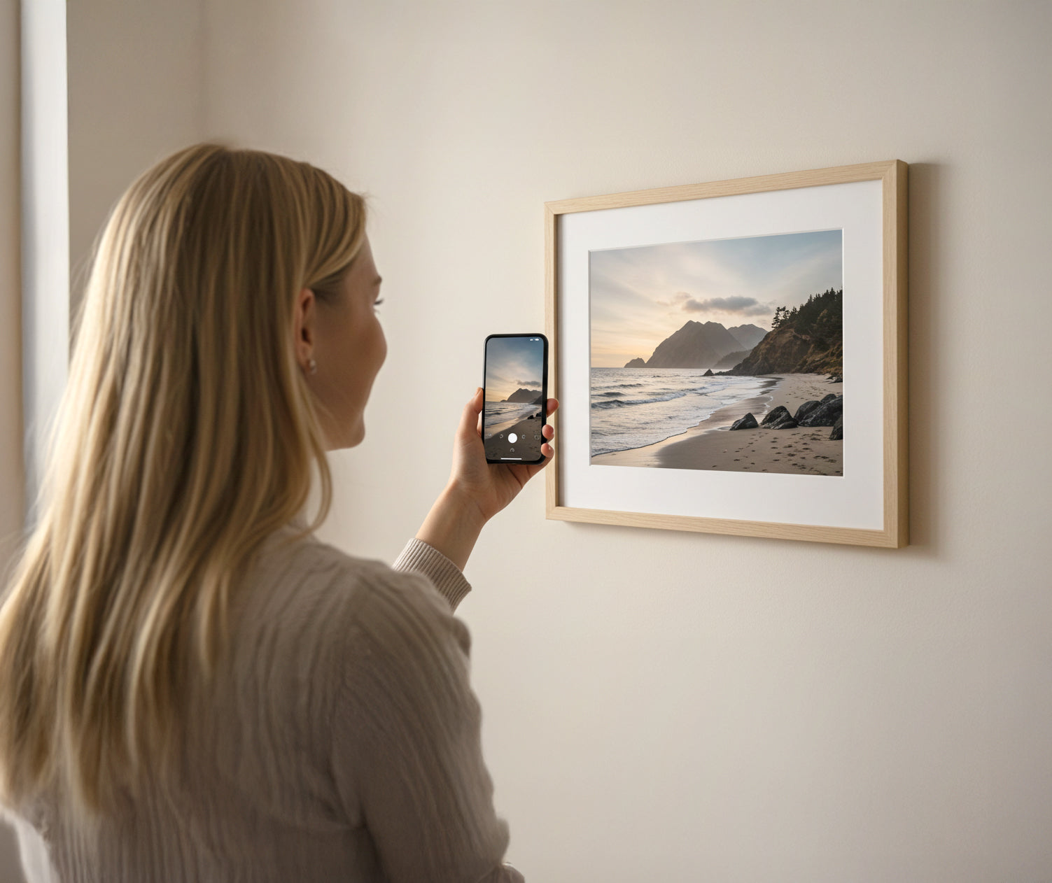 Blonde woman holding phone towards framed photo on wall – personalised fine art print made from mobile photo